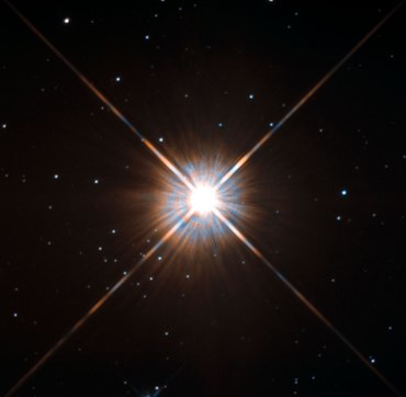  Hubble Space Telescope image is our closest stellar neighbour: Proxima Centauri, just over four light-years from Earth. Although it looks bright through the eye of Hubble, Proxima Centauri -- with only about one eight the mass of our sun -- is not visible to the naked eye.Shining brightly in this Hubble image is our closest stellar neighbour: Proxima Centauri. Proxima Centauri lies in the constellation of Centaurus (The Centaur), just over four light-years from Earth. Although it looks bright through the eye of Hubble, as you might expect from the nearest star to the Solar System, Proxima Centauri is not visible to the naked eye. Its average luminosity is very low, and it is quite small compared to other stars, at only about an eighth of the mass of the Sun. However, on occasion, its brightness increases. Proxima is what is known as a “flare star”, meaning that convection processes within the star’s body make it prone to random and dramatic changes in brightness. The convection processes not only trigger brilliant bursts of starlight but, combined with other factors, mean that Proxima Centauri is in for a very long life. Astronomers predict that this star will remain middle-aged — or a “main sequence” star in astronomical terms — for another four trillion years, some 300 times the age of the current Universe. These observations were taken using Hubble’s Wide Field and Planetary Camera 2 (WFPC2). Proxima Centauri is actually part of a triple star system — its two companions, Alpha Centauri A and B, lie out of frame. Although by cosmic standards it is a close neighbour, Proxima Centauri remains a point-like object even using Hubble’s eagle-eyed vision, hinting at the vast scale of the Universe around us.